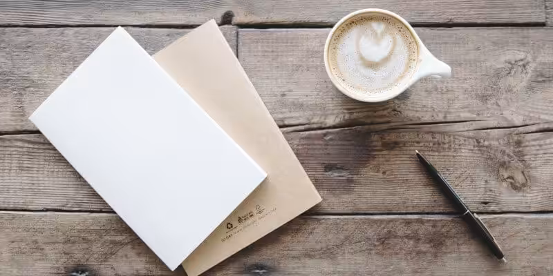 A coffee, pen, and a blank-paged book for notes on satisfice for your small business.