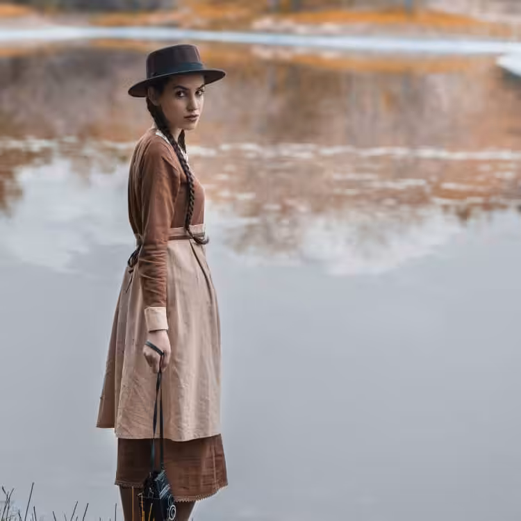 A contemplative woman in front of a lake, looking at the camera. 