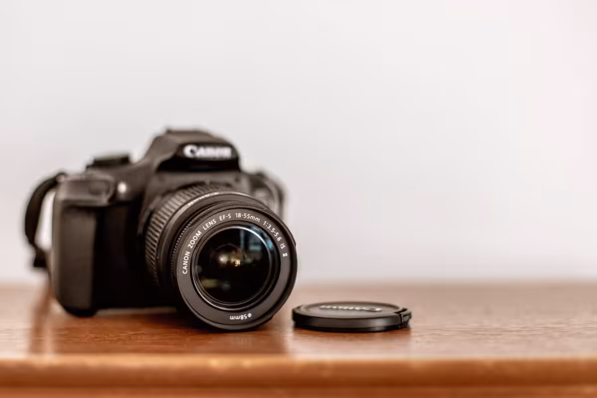 A Canon DSLR resting on a wooden table with the lens cap off.
