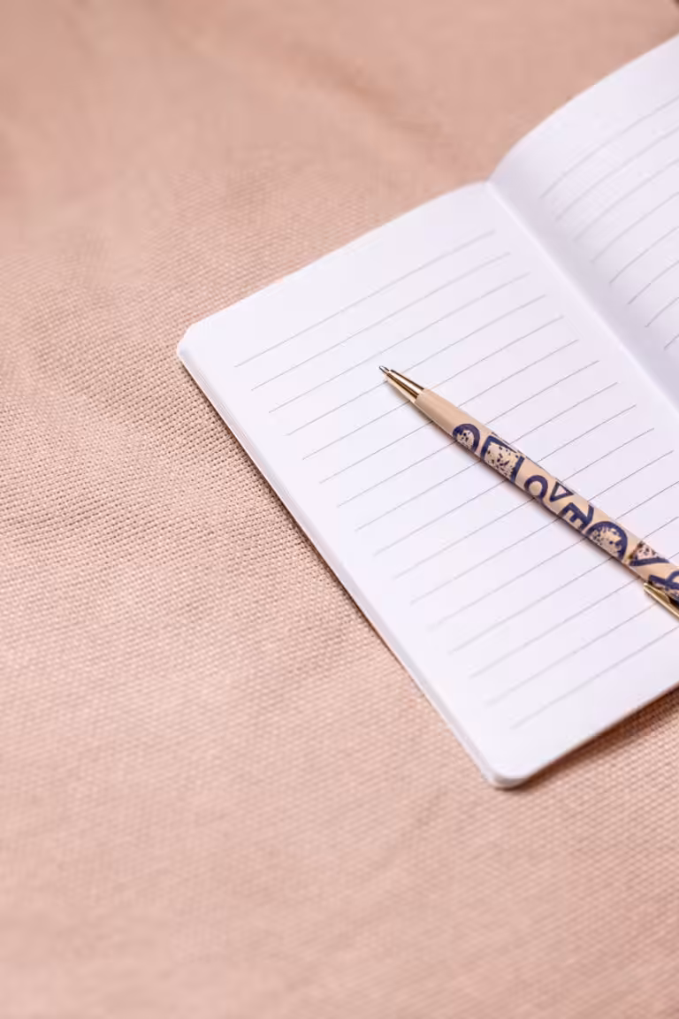 An open notebook with a pink pen on a pink fabric background.