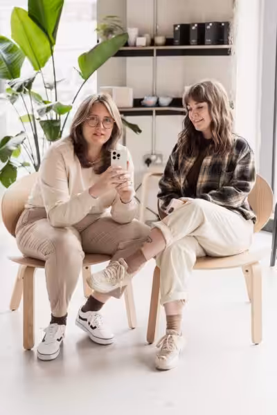 Studio Cotton's Aime sat with Lyzi and holding up an iPhone.