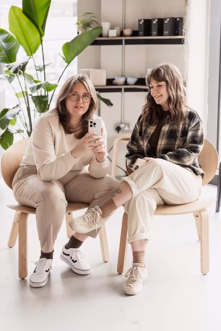 Studio Cotton's Aime sat with Lyzi and holding up an iPhone.