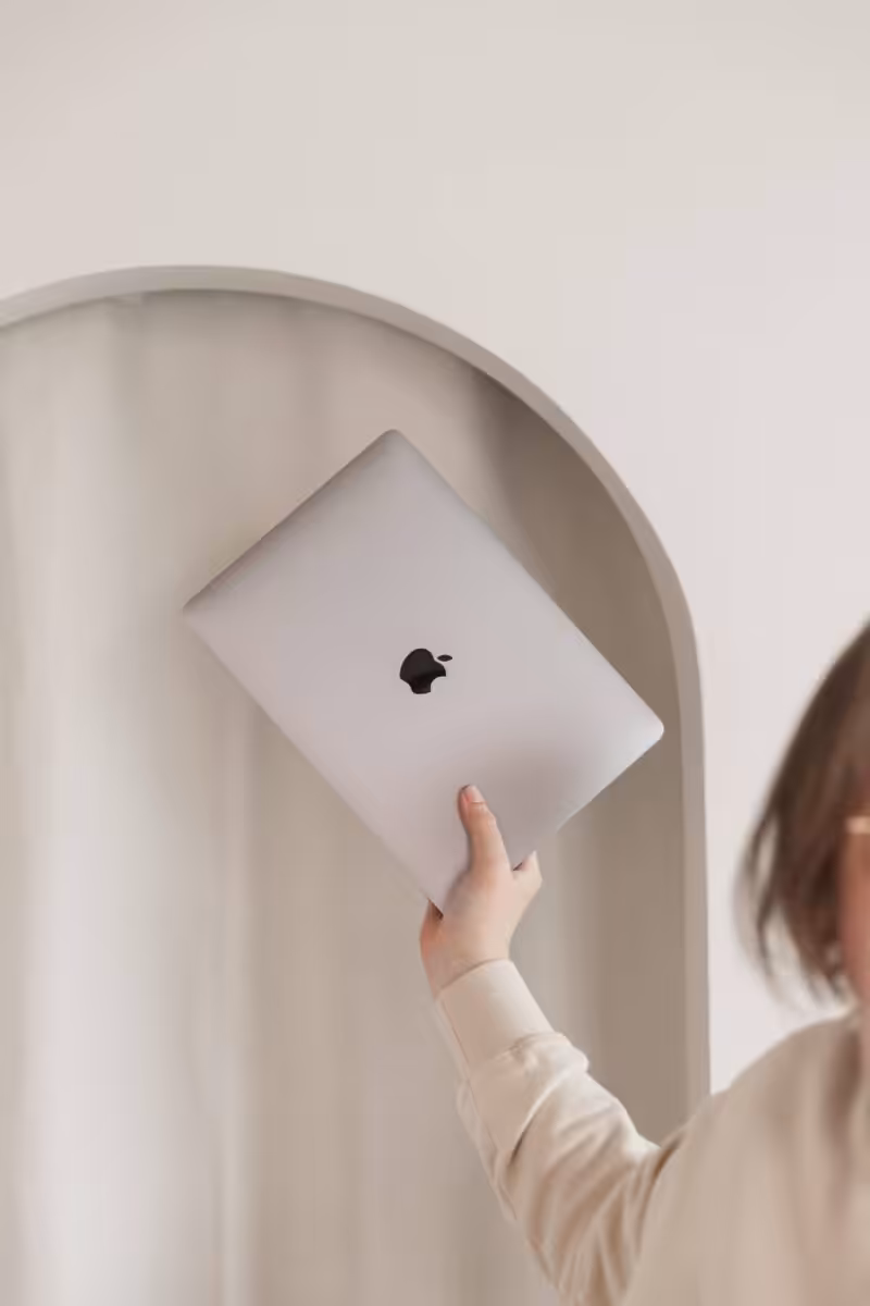 An Apple MacBook laptop being held up in Aime's hand under the archway interior at Greytone Coffee, Bristol.