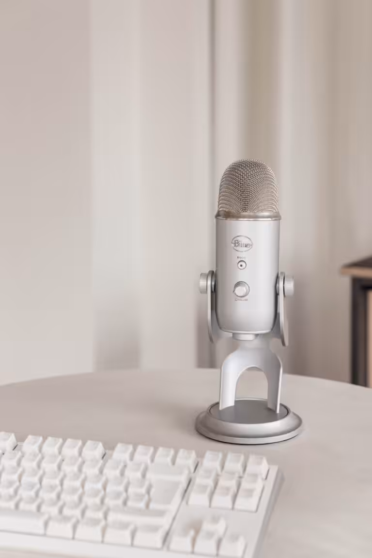 A silver microphone and white keyboard on a table against a white background
