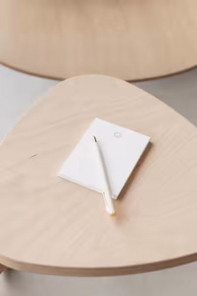 A notepad with a smiley face icon and a white pen placed on a wooden stool.