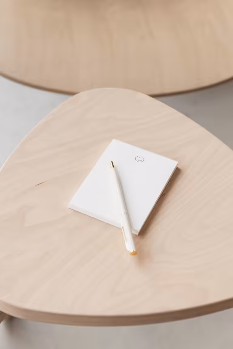 A notepad with a smiley face icon and a white pen placed on a wooden stool.