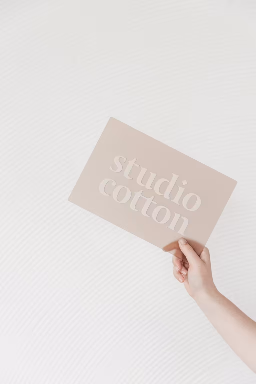 A sign of The Studio Cotton logo held up in one hand.