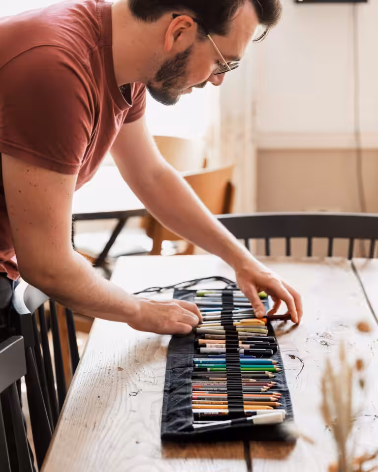 Artist materials being unravelled on a wooden table by man (Cai Burton)