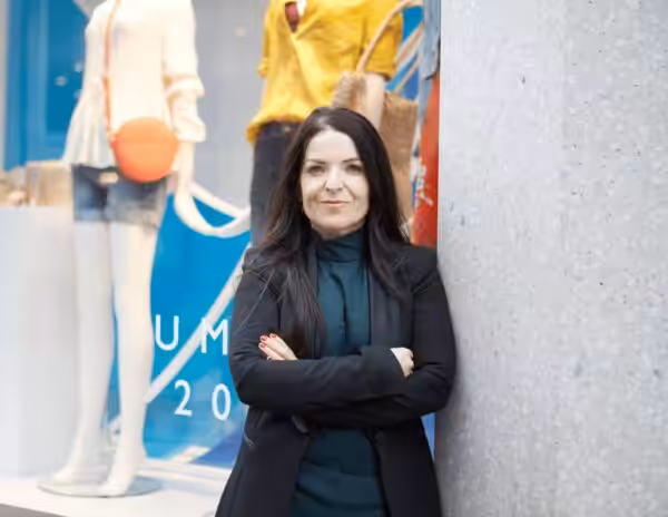 Nicole Higgins stands in front of a shop window with arms folded