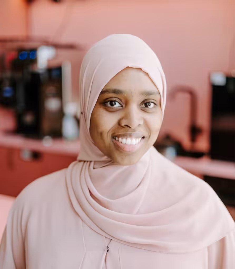 Eman wearing pale pink in front of a pink and black background