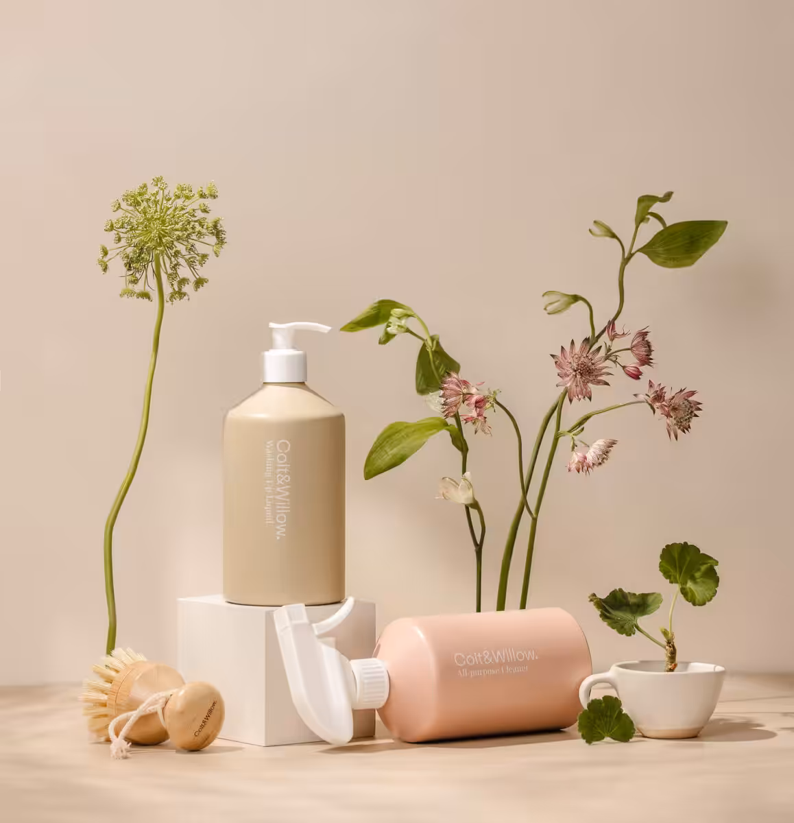 Beautiful lotion bottles and modern flower arrangement on a beige background