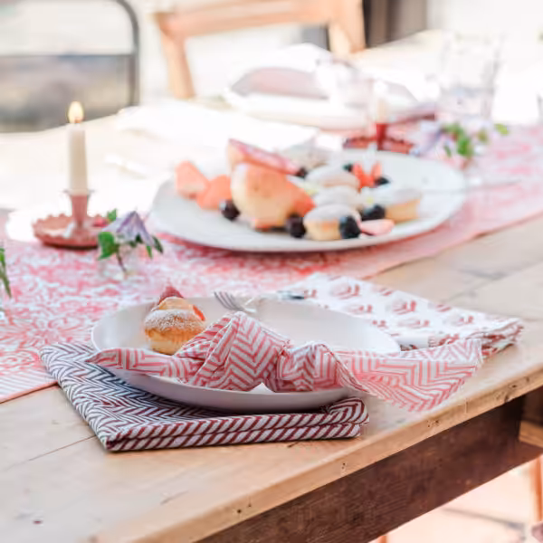 Table with hand printed table runner and napkins, with food and candles in the background