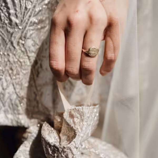 Close up of a gold ring on the ring finger of a hand, with crumpled metallic fabric background