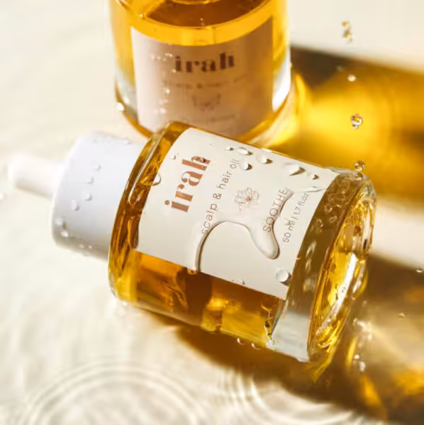 Bottles of glowy yellow Irah hair oil in shallow water with drips