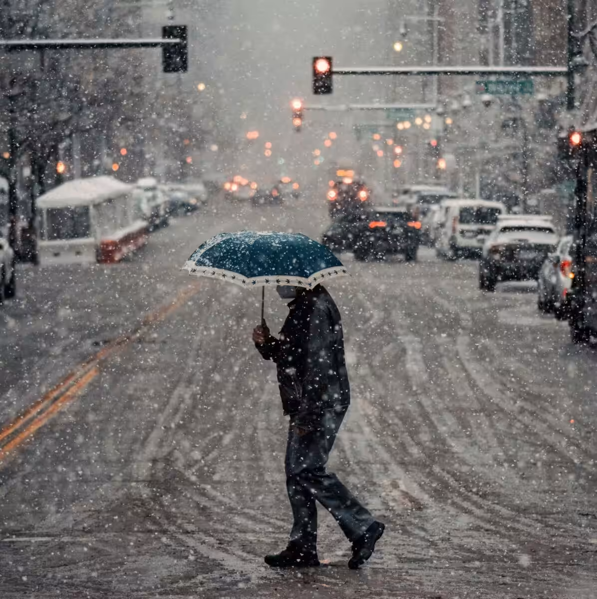 A person holding an umbrella and crossing the road in a blizzard
